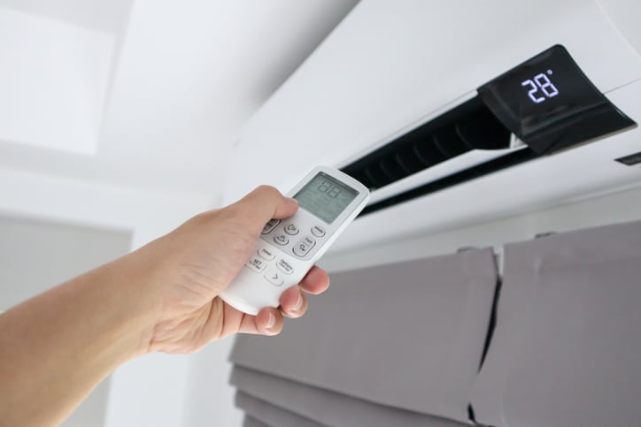 Hand with remote control directed on air conditioner plancher-chauffant-hansez-roggeman-belgique