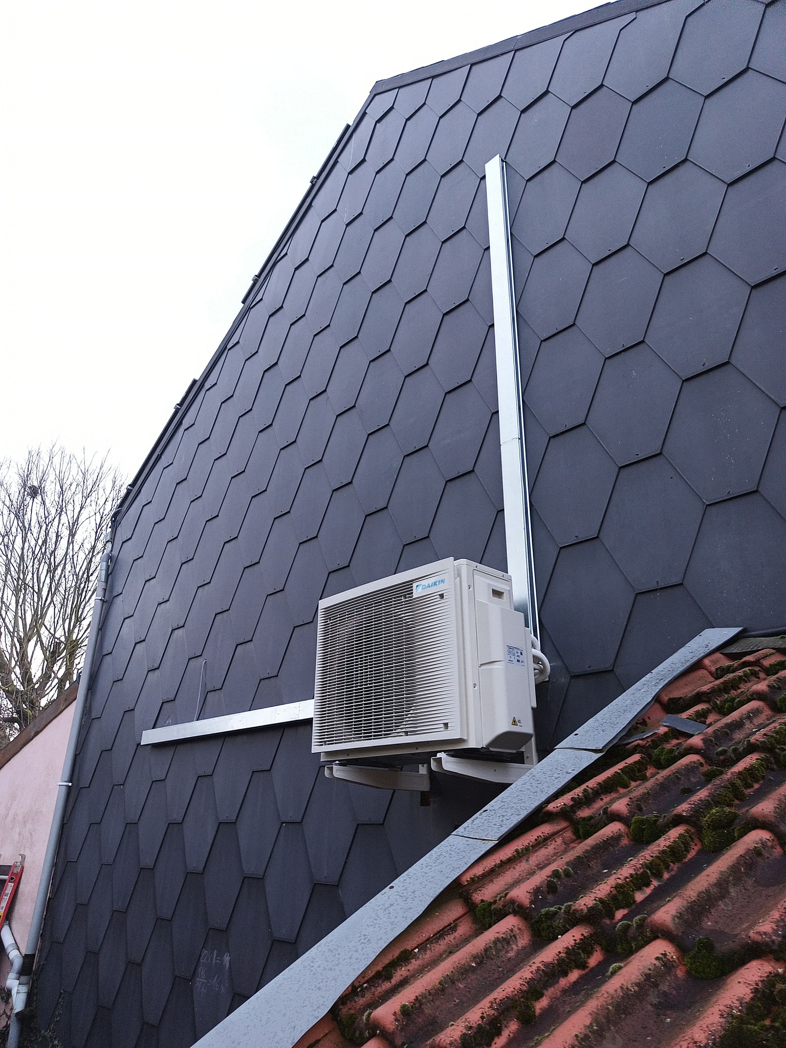 Unité extérieure climatisation pompe à chaleur Daikin installation façade inclinée toiture ardoises hexagonales