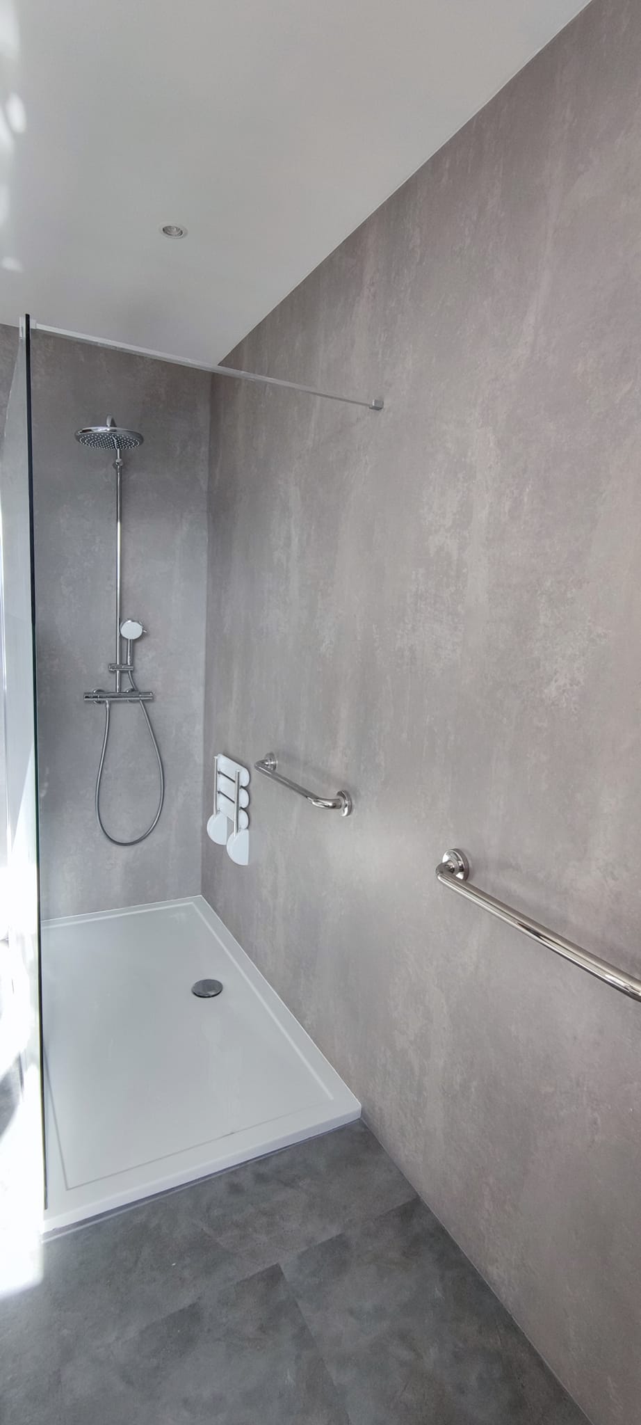 Douche à l'italienne accessible murs effet béton ciré barre d'appui sécurité salle de bain